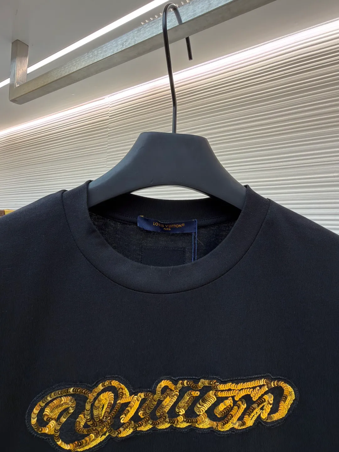 LOUIS VUITTON cotton round neck embroidered Vuitton signature logo short sleeves ●Original version: purchased and developed for 12300 ●Item number: 1682273-A10 ●Fabric: cotton fabric ●Technology: embroidery production ●Color: black ●Version: fitted version ●Weight: about 295 grams ●Size: S-M-L-XL ●Description: This white short-sleeved T-shirt is made of high-count combed cotton fabric and has been treated with pre-washing technology. It has a soft and skin-friendly touch and is not easy to deform. The silhouette of the shirt is a loose shoulder design, which meets the needs of modern casual wear. The core decoration area on the chest uses hand-beading and bronzing technology, and uses metallic gold sequins and embroidery threads intertwined to outline a three-dimensional letter pattern. The sequins are layered and inlaid, and each one is manually positioned and fixed by craftsmen to ensure a regular texture and uniform gloss. The edges of the letters are sewn with matte silk thread to form a visual contrast between gold and matte, while reinforcing the decorative structure to avoid falling off during wear. The neckline uses double-needle hemming technology and is matched with ribbed cuffs of the same fabric. It is durable and fits the neck. The overall craftsmanship combines handicraftsmanship with modern clothing technology, and the details show exquisite texture. The overall wiring is straight and delicate, the fabric is comfortable and soft, and the color is consistent without color difference. It can be matched with the same style to create a fashionable look and control various occasions. Customized accessories, complete with three standards, same style for men and women!